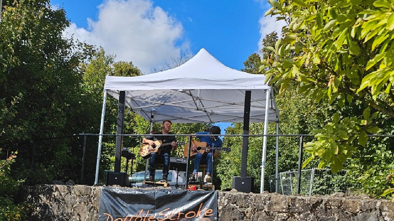 Zwei Musiker mit Akustikgitarren unter einem Sonnendach.