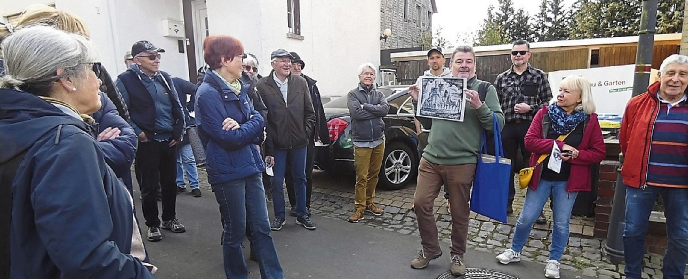 In einem Kreis interessierter Personen steht Volker Hess und zeigt eine Abbildung.
